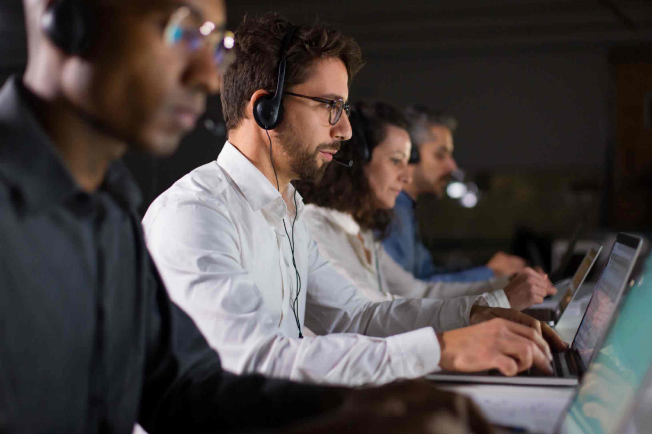 A diverse team of professionals working in a call center, wearing headsets and assisting customers.