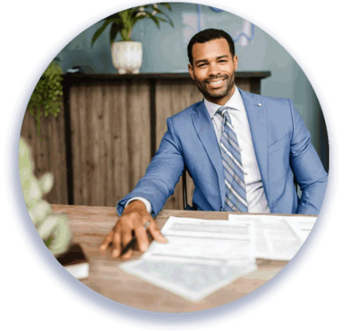 A man in a suit working at a desk with a laptop and papers.