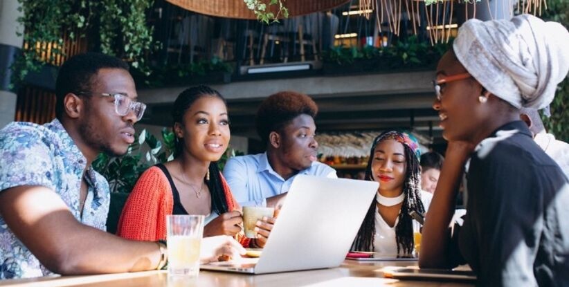 Young individuals gathered around a table, working together on a laptop.